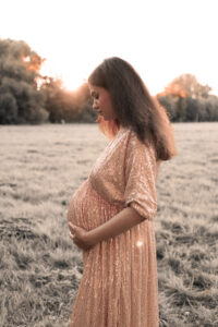 babybauch-sonnenuntergang-fuerth Schwangere Frau hält Babybauch auf Wiese im Sonnenuntergang in Fürth.