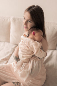 babyfotos-nuernberg Frau sitzt auf Sofa, hält ihr neugeborenes Baby in Armen und lächelt in Nürnberg.