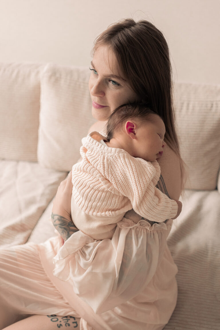 Frau sitzt auf Sofa, hält ihr neugeborenes Baby in Armen und lächelt in Nürnberg.