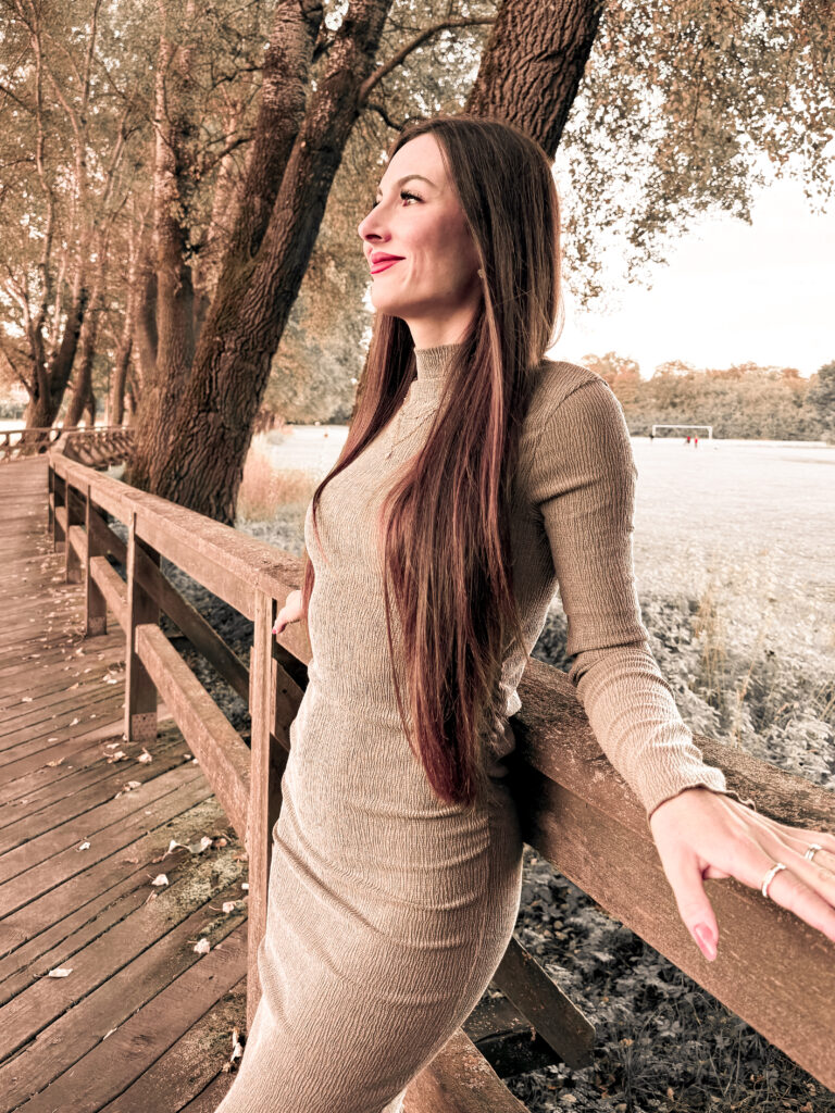 Lächelnde Frau auf einer Brücke legt Hand auf das Geländer.