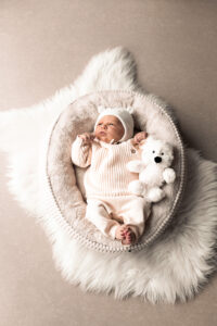 neugeborenenfotos-nuernberg Baby liegt auf Kuscheldecke mit Teddybär und blickt nach oben.