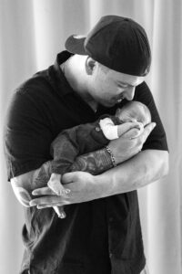 newborn- fotografie-nuernberg Mann hält Neugeborenes im Arm, küsst es und sieht es an in Nürnberg.