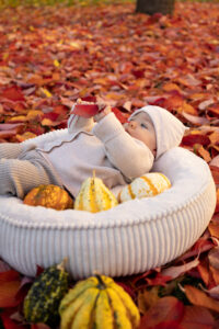 newborn-portrait-fuerth Baby liegt auf Blätterhaufen und spielt auf Wiese in Fürth.