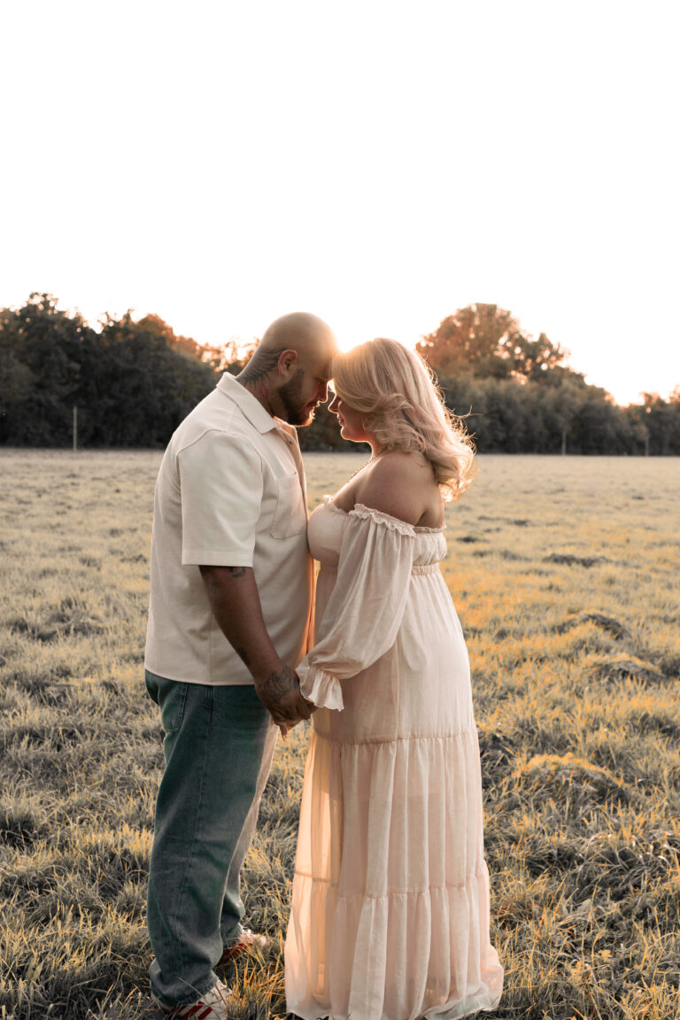 Ein Paar steht auf einer Wiese im Sonnenuntergang und legen ihre Stirn aneinander.