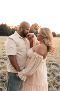 paarshooting-sonnenuntergang-fuerth Ein Mann steht auf einer Wiese im Sonnenuntergang und hält ihre Hand und küsst sie.