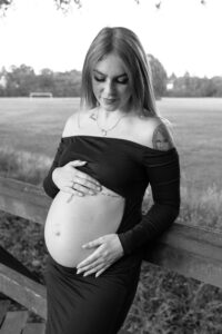 schwangerschaft-natuerlich-fuerth Schwangere Frau auf einer Brücke in Fürth hält ihren Babybauch und blickt nach unten.