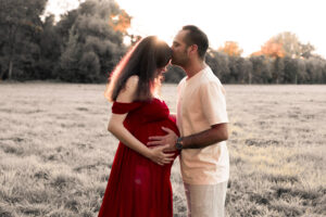 schwangerschaft-paar-fuerth Paar steht auf Wiese in Fürth, Mann küsst die Stirn der schwangeren Frau und hält ihren Babybauch fest.