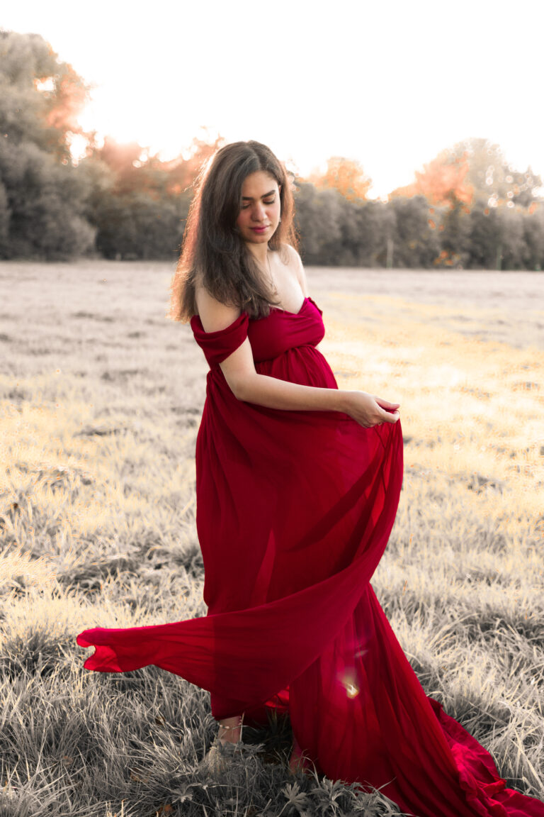 Frau auf Wiese trägt rotes Kleid und schwingt es mit der Hand, Blick nach unten.